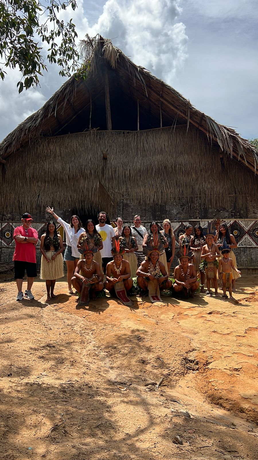 Indigenous community gathered in front of a traditional thatched house