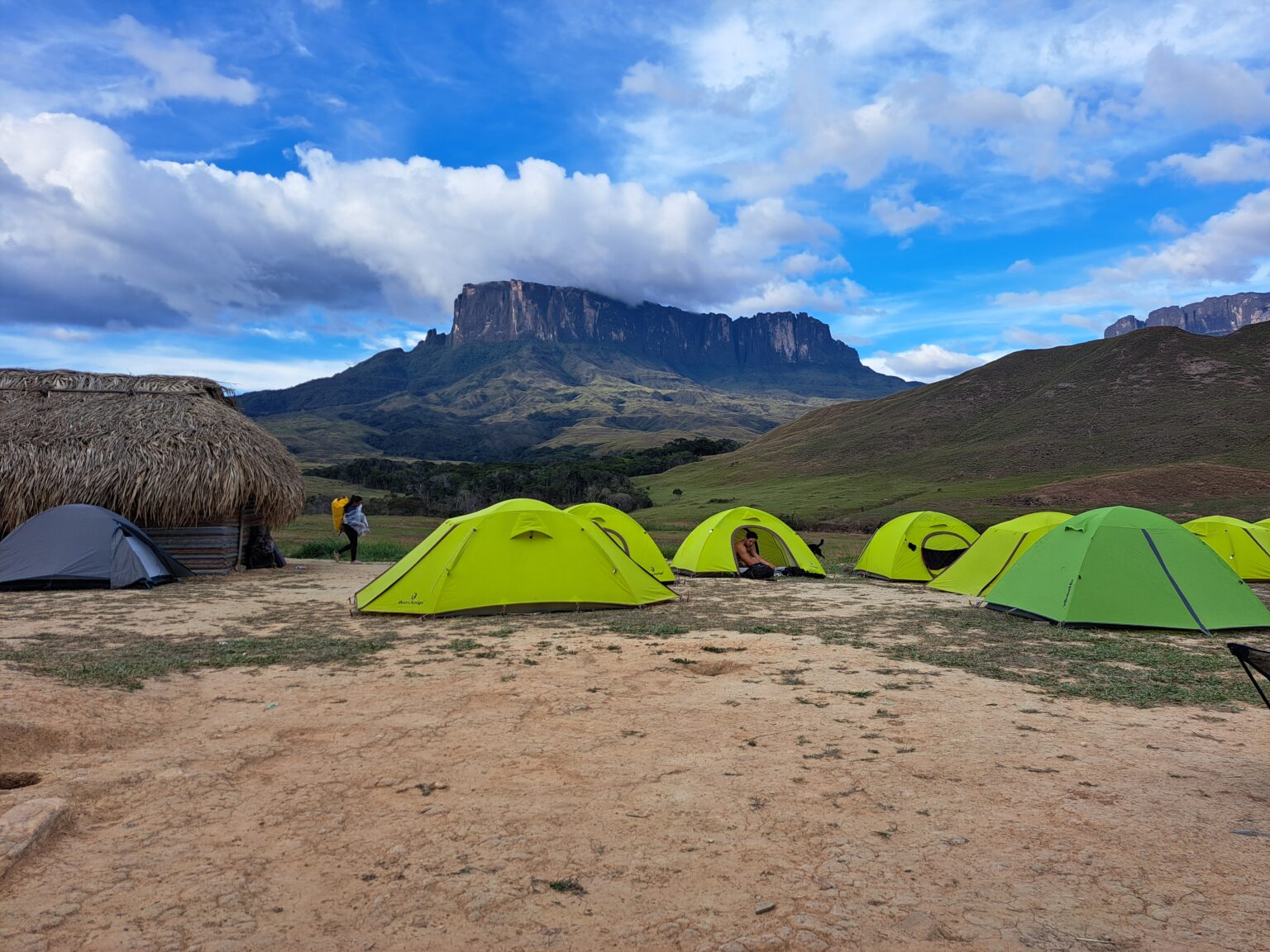 Green tents at a base camp with the table-top Mount Roraima on the horizon