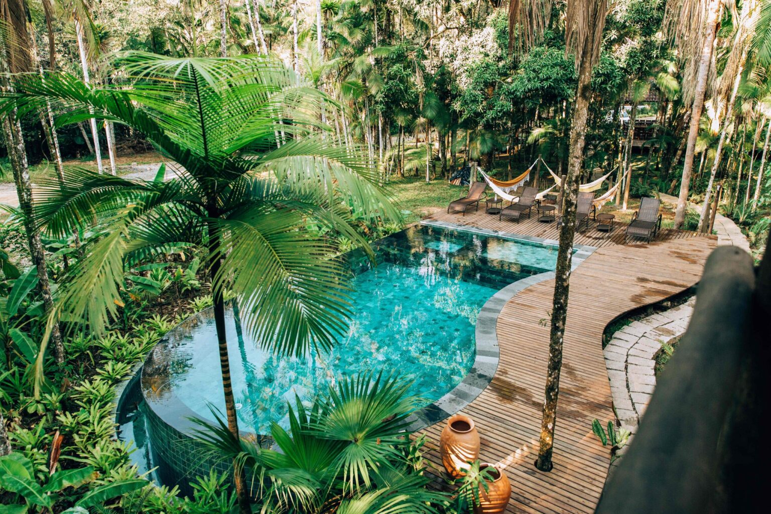 Pool surrounded by palm trees and wooden decks at Glamping Mangarito in the Atlantic Forest